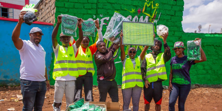 Shorten this: From left: Stephen Maundu, Territory Business Lead, Nairobi at Safaricom PLC, hands over football kits to Denis Odhiambo of Young Cranes 4B, Verah Adhiambo of Beijing Raisers F.C, Peter Njogu, Chairman of Kambi Safi Community representing the four football teams, Tina Tune of Flames F.C and Kevin Irungu of True Colours, assisted by Susan Muthoka from the Youth Segment at Safaricom PLC. The handover ceremony was held at Mcedo Beijing School Grounds in Mathare during a seven-a-side football tournament organized by Safaricom Hook.